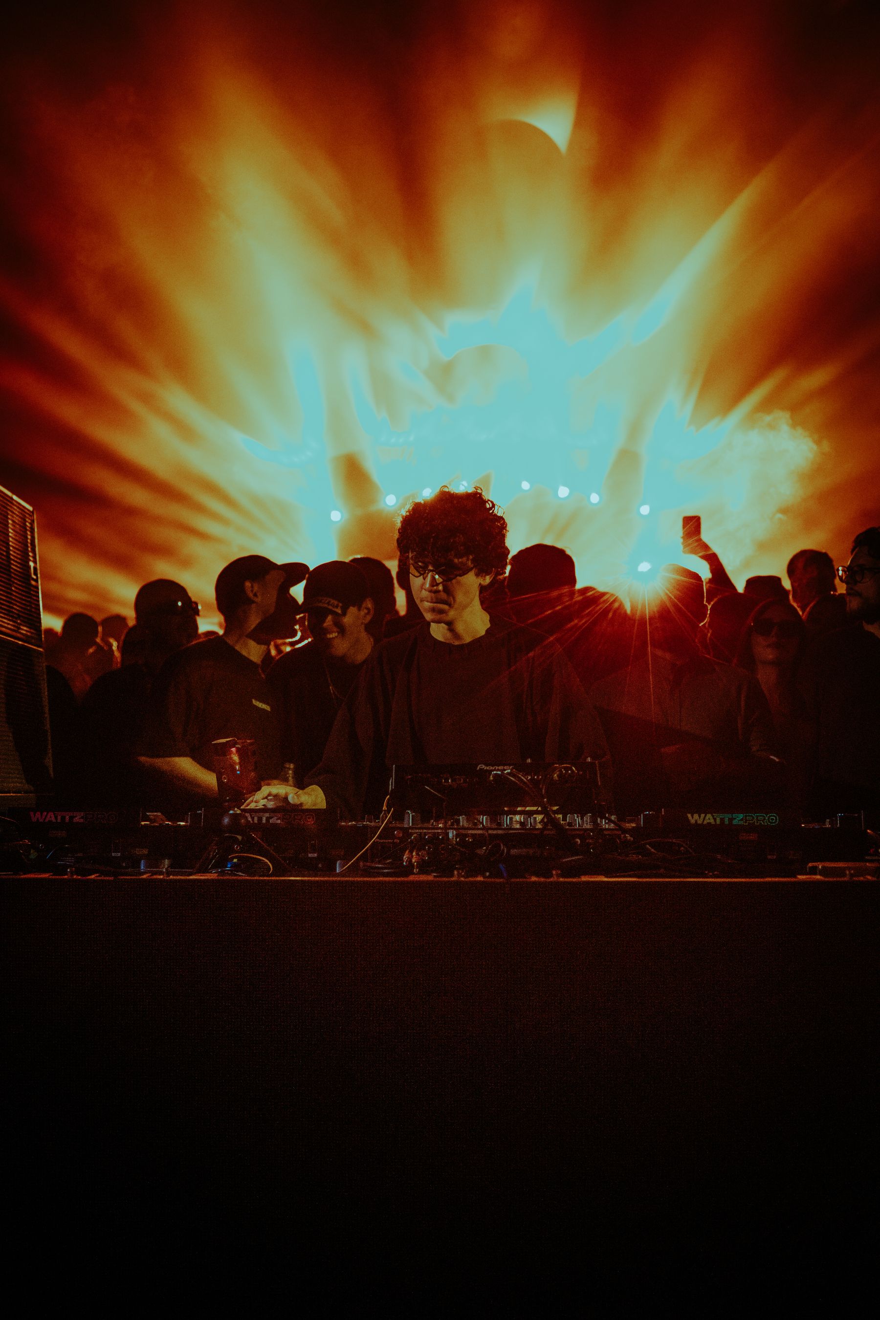 DJ performing beneath vivid lights at a packed event