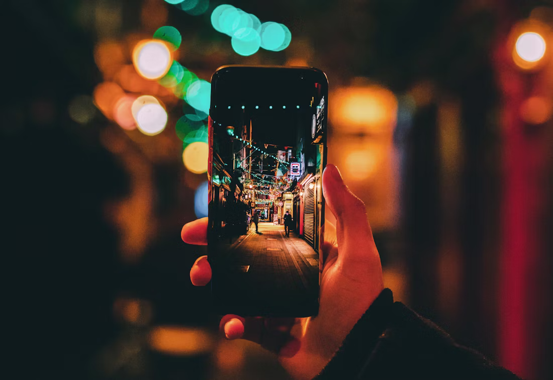 Hand holding a smartphone on a city street at night