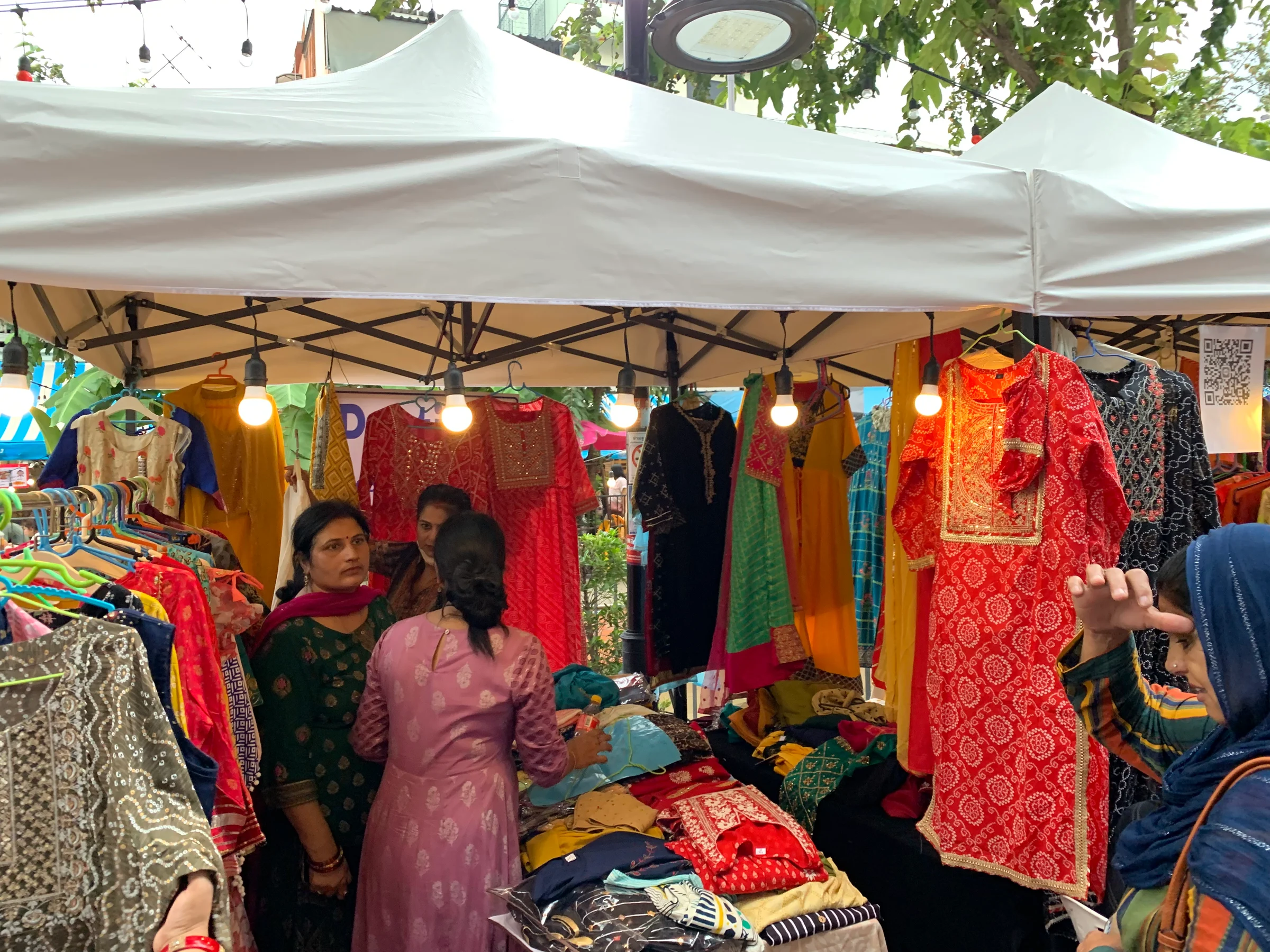 Colourful Indian clothing and fabrics hanging under a white market tent with string lights at a Deepavali celebration by Khlong Ong Ang in Bangkok