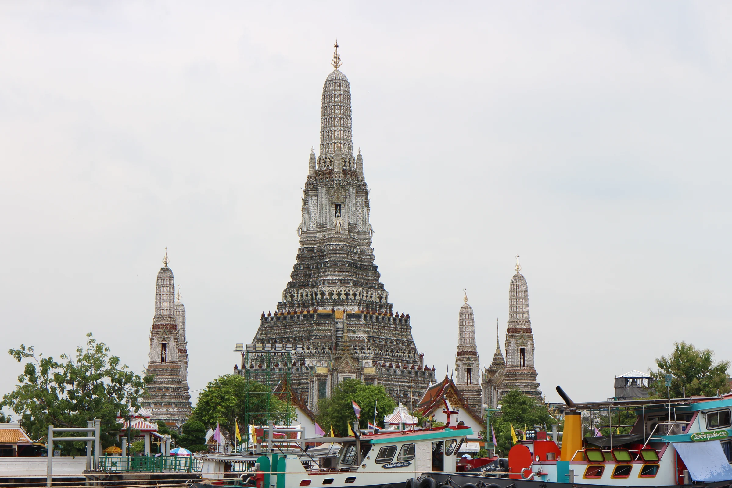 Wat Arun's central prang and smaller spires seen across the Chao Phraya River, with colourful river boats in the foreground