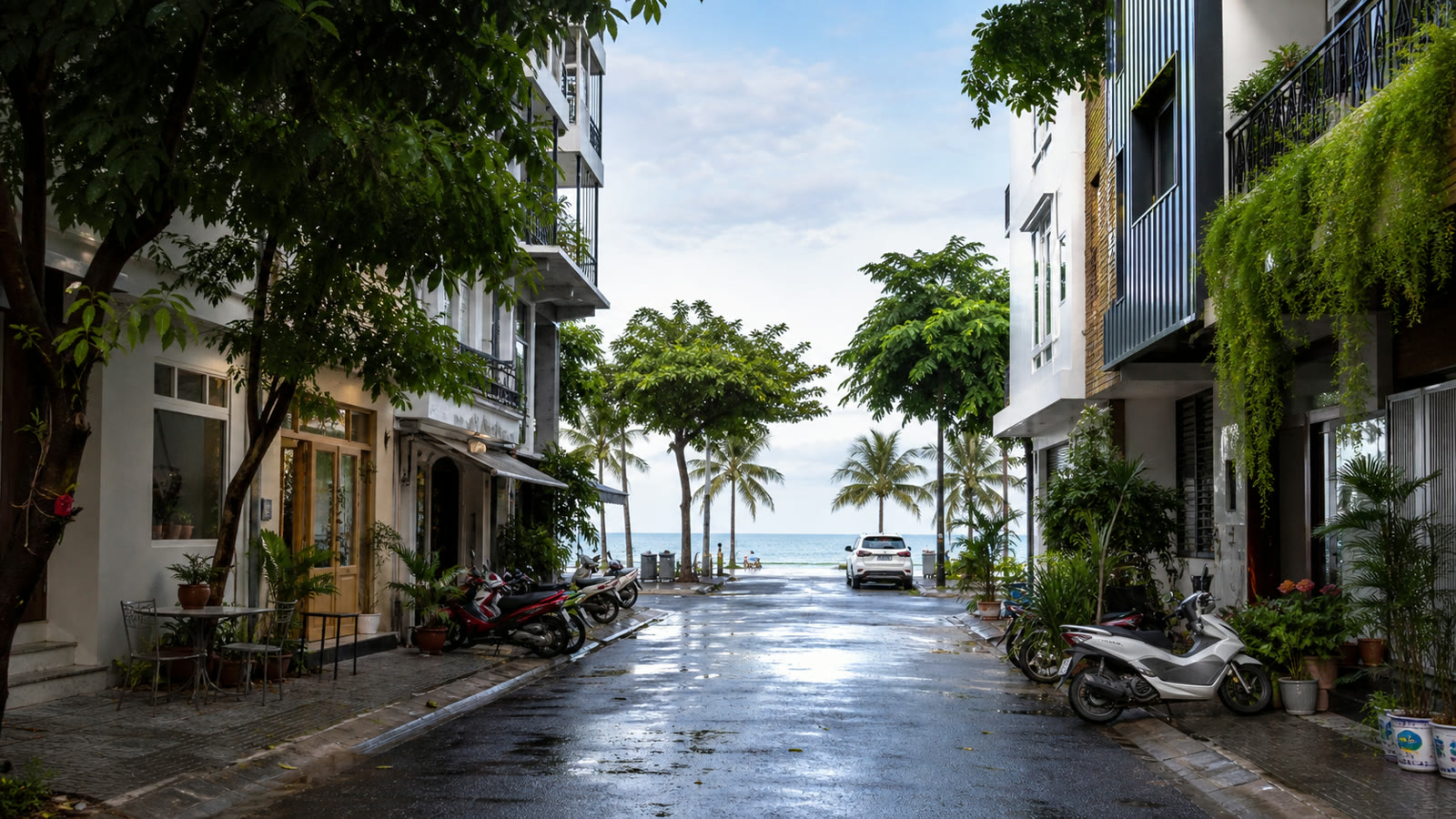 A leafy residential street in coastal Da Nang with apartments, scooters and the sea ahead