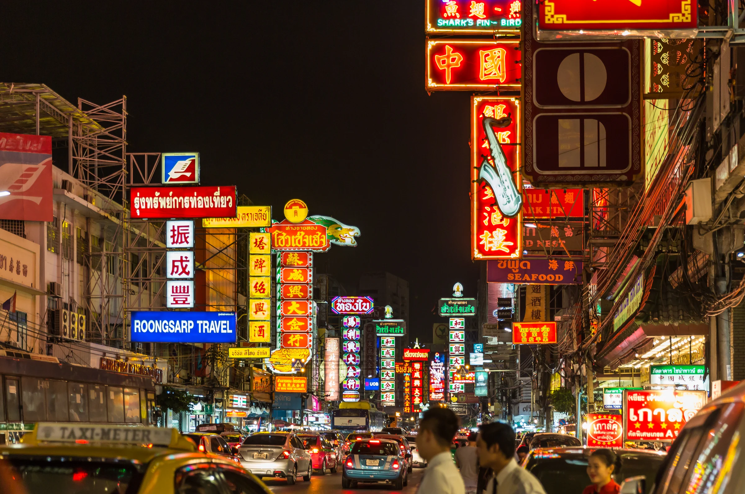 Yaowarat Road in Bangkok's Chinatown at night, lined with red, yellow and neon shop signs above traffic and pedestrians